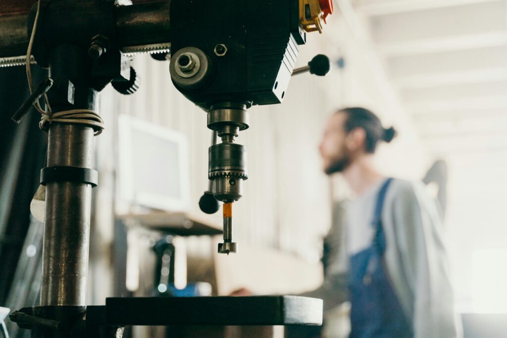 A factory worker stands near machinery in an industrial workshop setting.